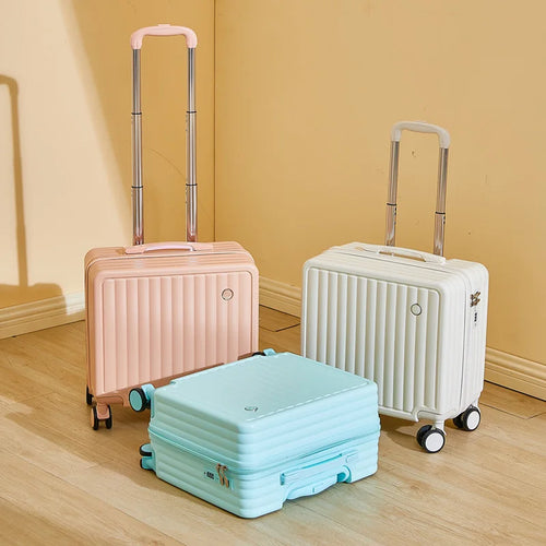 Three suitcases in pink, white, and blue on a wooden floor with a beige wall background.
