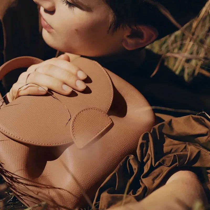 Person holding a brown leather handbag with a floral background