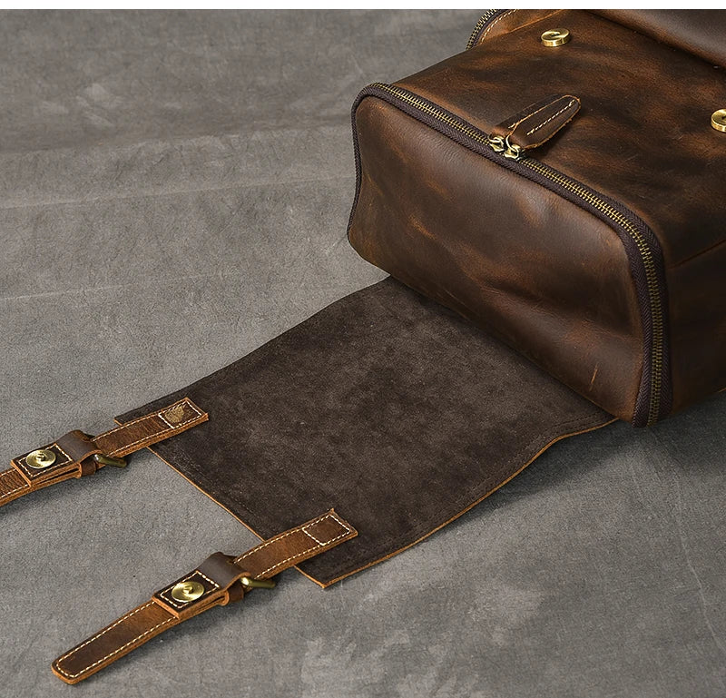 Brown leather duffel bag with gold zippers on a gray surface