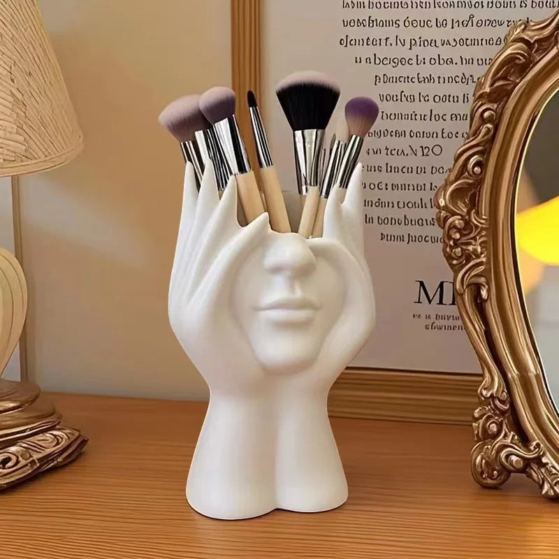 White hand-shaped brush holder with makeup brushes on a wooden surface.