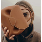 Person holding a brown leather handbag with a heart design.