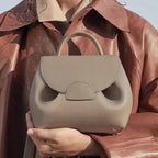 Person holding a beige handbag with a brown leather jacket