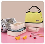Lunch box set with pink container, silver lid, and yellow bag on a pink surface.