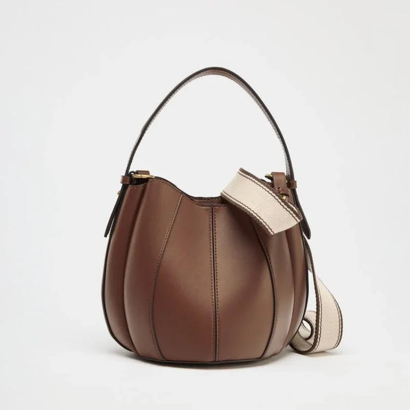 Brown leather handbag with a beige strap on a light gray background