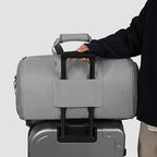 Person holding a gray duffel bag over a suitcase on a light gray background